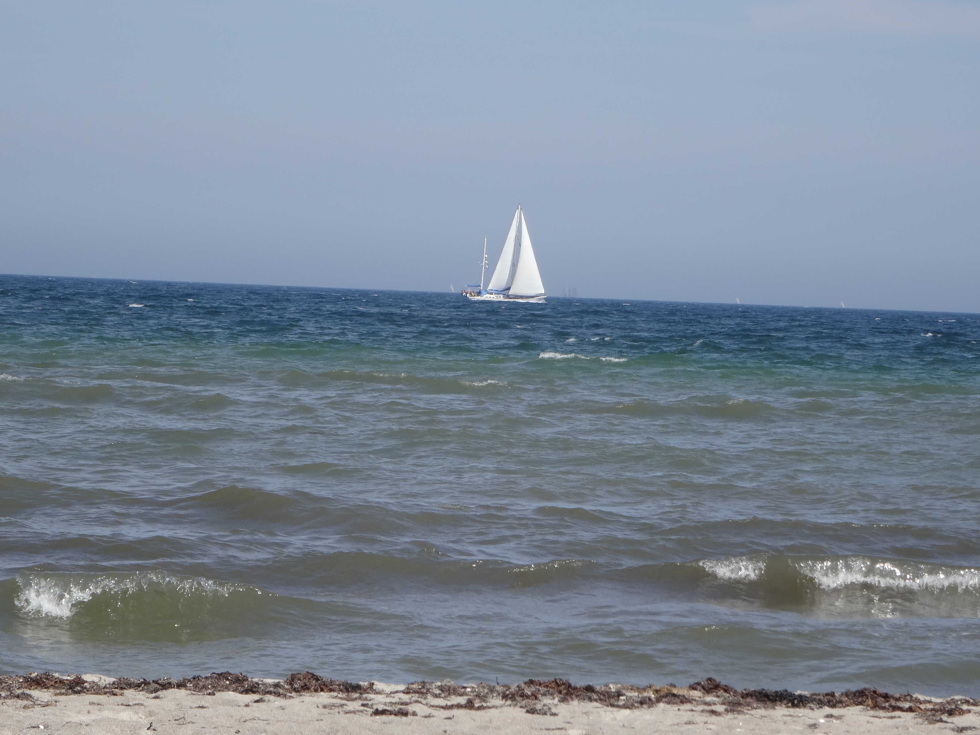 Une plage avec des vagues et un voilier à l’horizon.