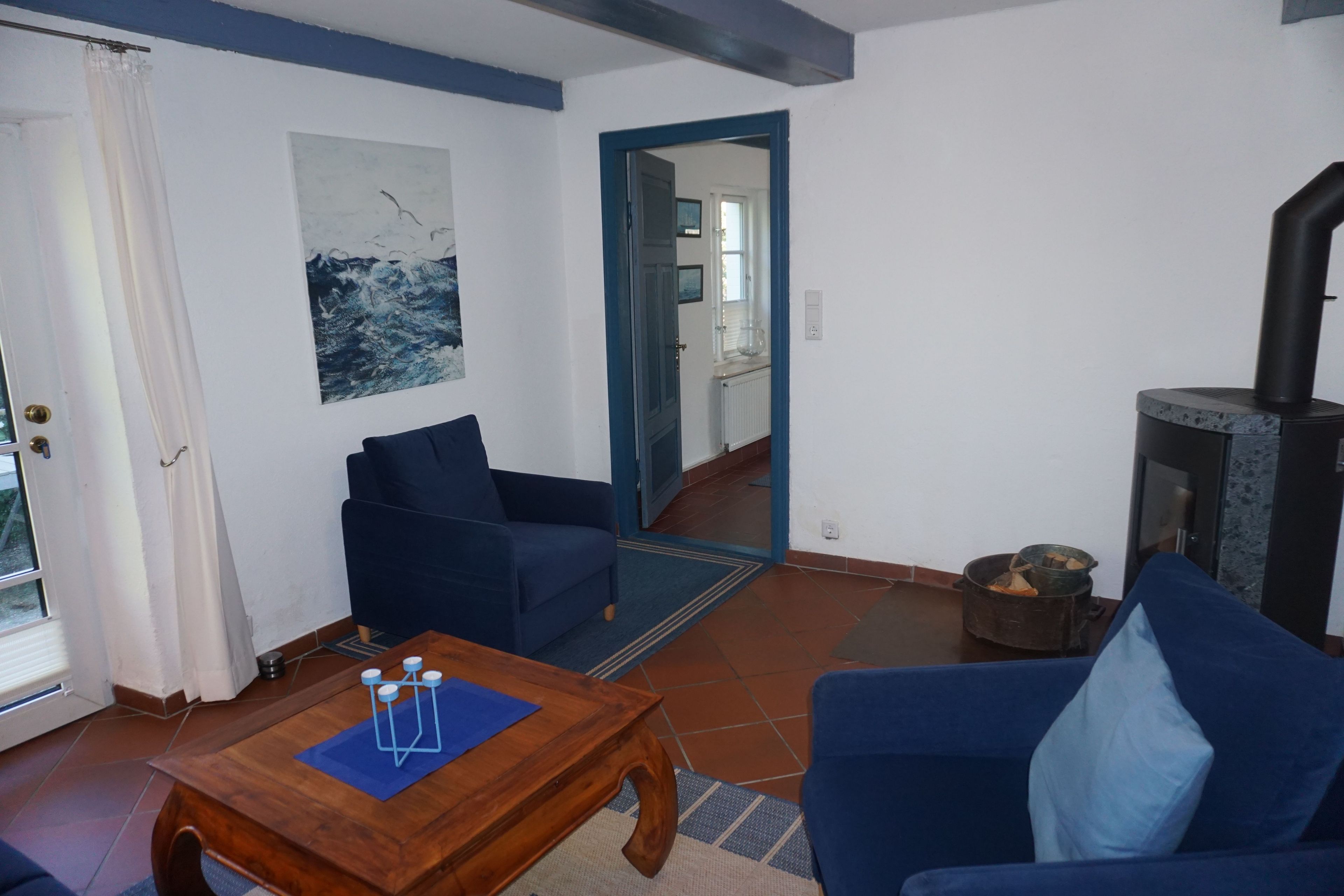 Una sala de estar con un sofá azul, una mesa de centro de madera, una chimenea y vistas a otra habitación a través de un vano.