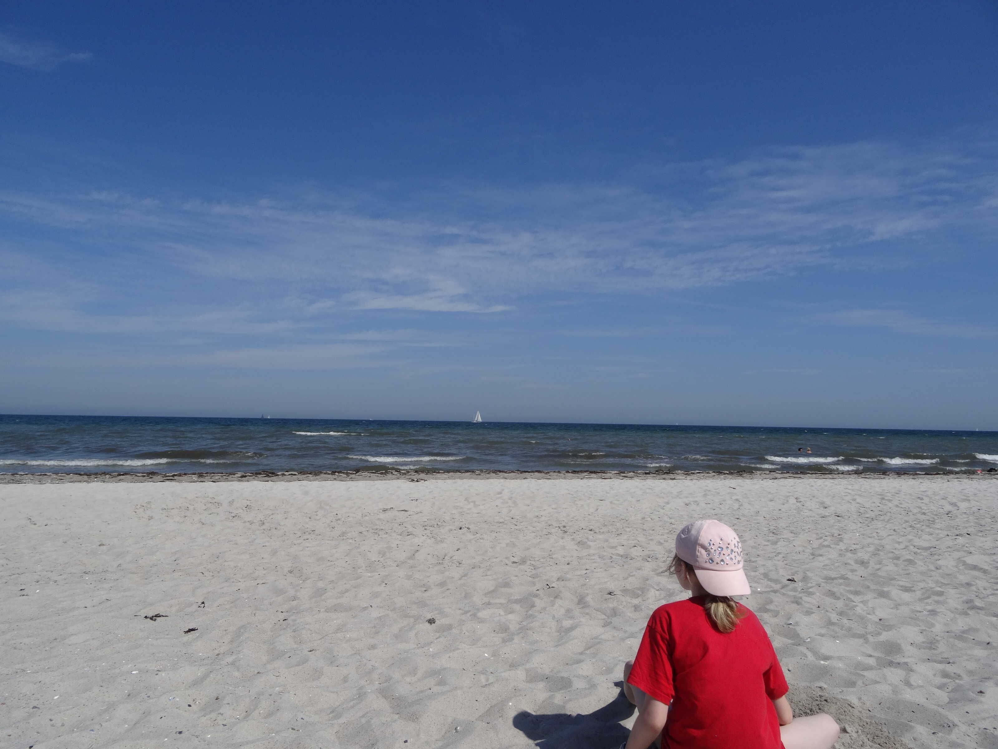 A beach with a person sitting on the sand, facing the ocean.