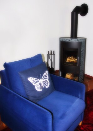 A blue armchair with a butterfly pillow, a black fireplace, and a red patterned rug. - FW Geltinger Birk - Luckow Georg Asmussen Haus (Pommerby)