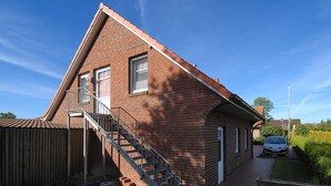 Een bakstenen gebouw met een schuin dak, een trap die naar een deur leidt, en een auto op de oprit.