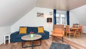Een moderne woonkamer met een blauwe bank, een houten salontafel, en een eethoek met een tafel en stoelen.