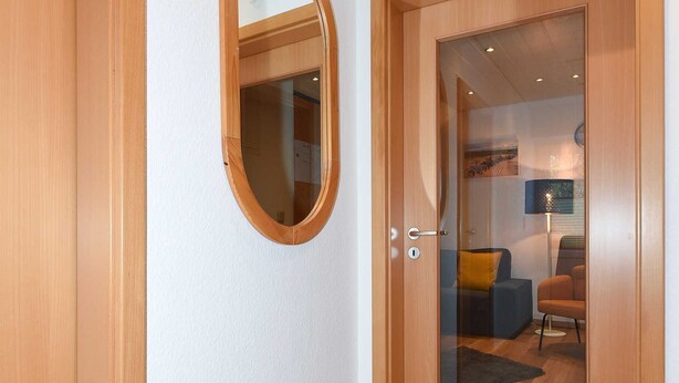 Een gang met een houten deur, een glazen deur en een spiegel aan de muur.