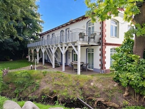 Una casa de dos pisos con un balcón, un patio cubierto y un jardín.