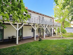 Un edificio de dos pisos con balcón, asientos al aire libre y una escalera que lleva al nivel superior.