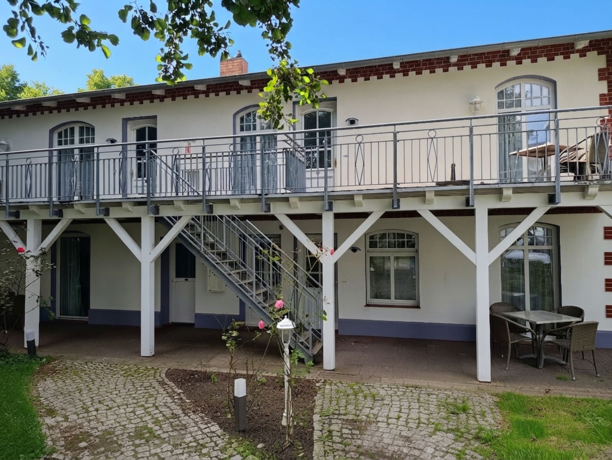 Ein zweistöckiges Gebäude mit Balkon, Treppe und Garten.