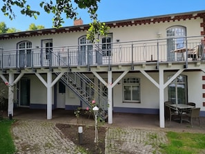 Un edificio de dos pisos con un balcón, una escalera y un jardín.