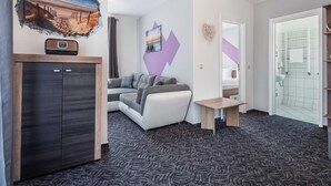 Ein modernes Wohnzimmer mit einer Couch, einem kleinen Tisch, einem Schrank und einer Wand mit Strandmotiv und geometrischen Formen.