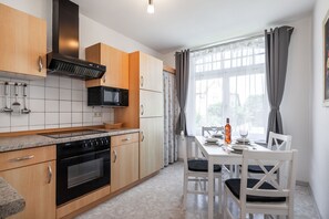 A modern kitchen with wooden cabinets, a built-in microwave, and a dining area with white chairs and a table set for two.