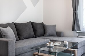 A modern living room with a grey sofa, a glass coffee table, and a window with curtains.
