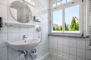 A modern bathroom with a white sink, mirror, and window.