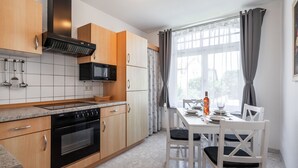 Une cuisine moderne avec des meubles en bois, un four à micro-ondes encastré et un coin repas avec des chaises blanches et une table dressée pour deux personnes.