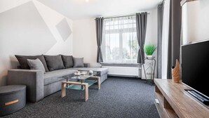 En moderne stue med en grå sofa, et glasbord og et fladskærms-tv på et træstel.