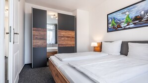 Une chambre d’hôtel avec un lit, un tableau, une table de chevet et une porte donnant sur une autre pièce.