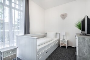 A minimalist bedroom with a single bed, a nightstand, a TV, and a heart-shaped wall decoration.