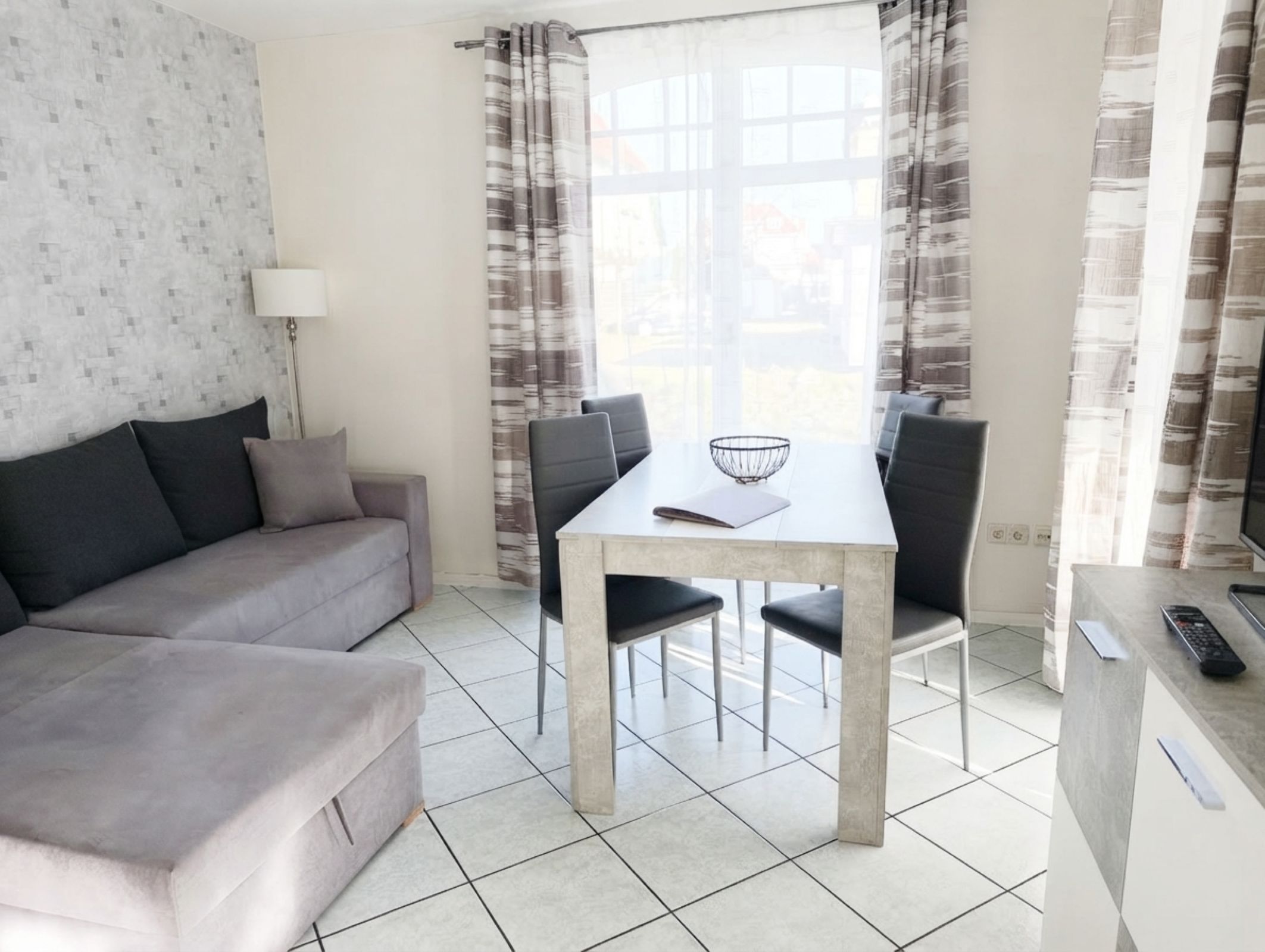 A modern living room with a sofa, dining table, chairs, and a kitchen area with a counter and appliances.