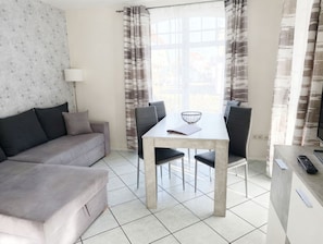 Uma sala de estar moderna com sofá, mesa de jantar, cadeiras e cozinha equipada com bancada e eletrodomésticos.