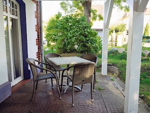 Um pátio externo com mesa e cadeiras, rodeado por vegetação e um caminho de tijolos.