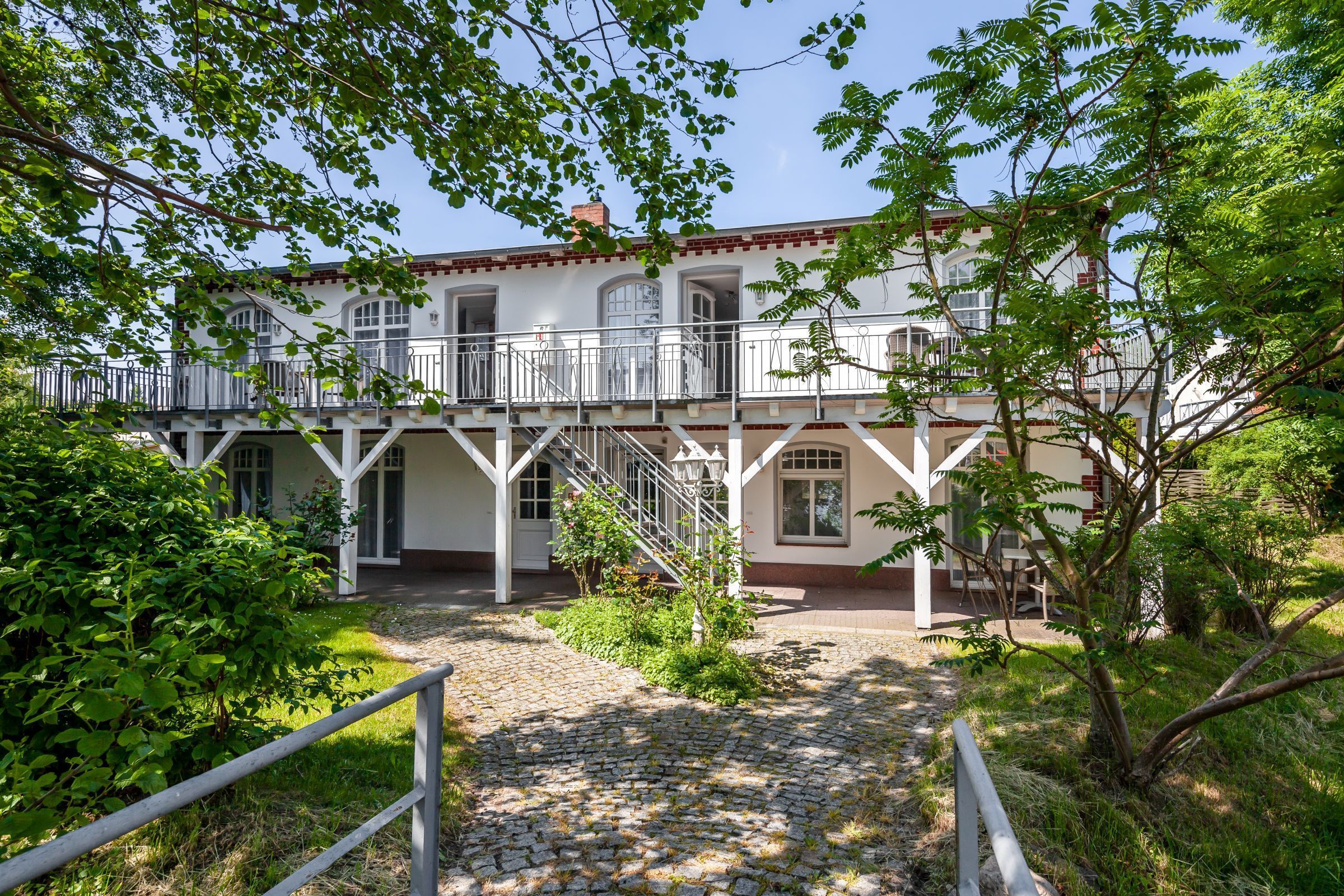A building with a white facade, a balcony, and a stone pathway leading to the entrance.