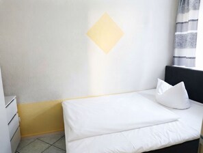 A hotel room with a bed, a nightstand, a wall-mounted light, and a window with curtains.