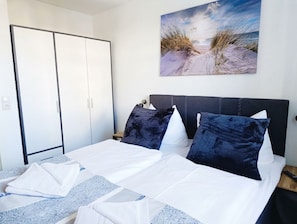 Quarto com cama, almofadas, guarda-roupa e um quadro na parede.