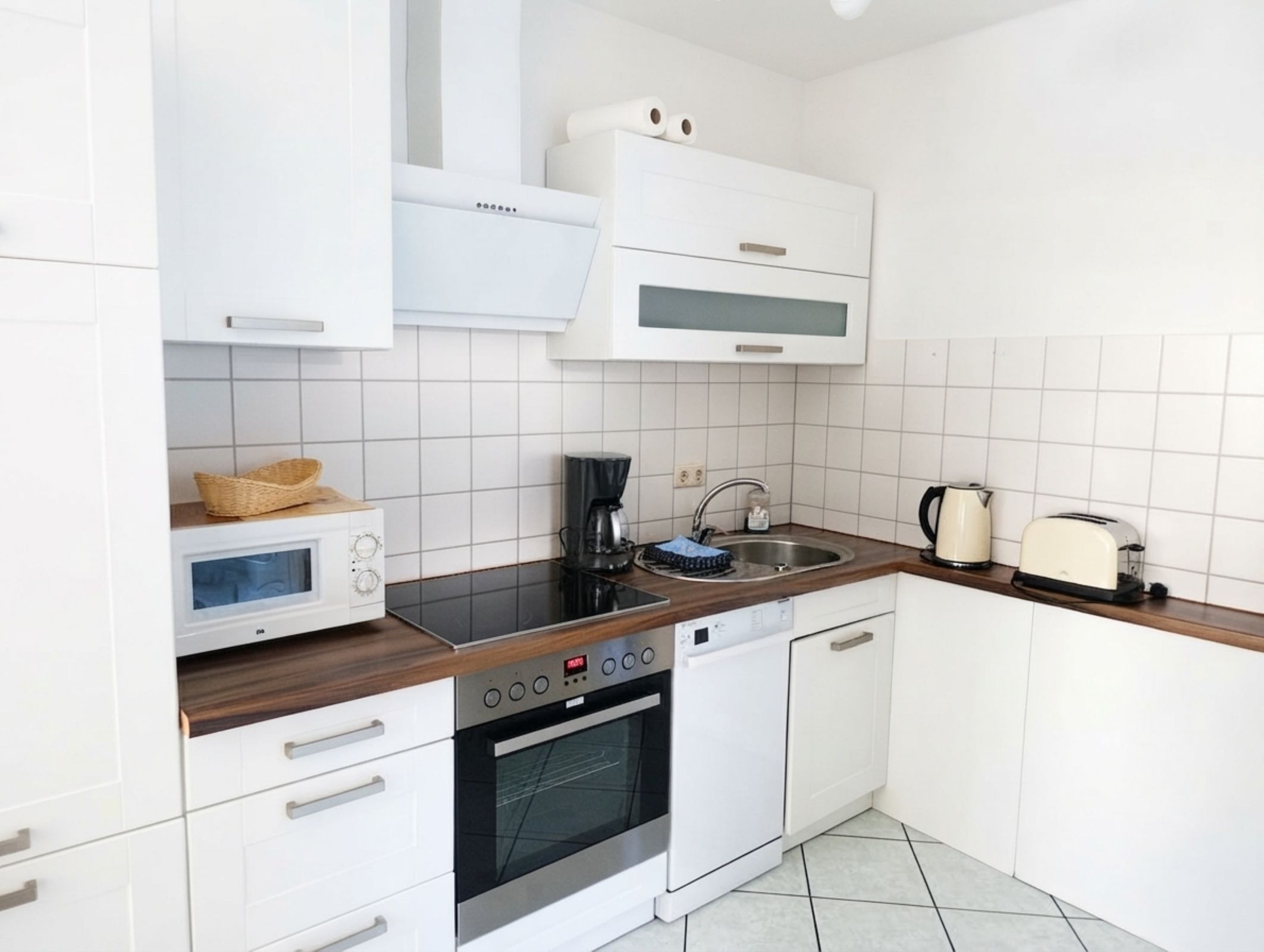 Una cocina moderna con armarios blancos, microondas, estufa, lavabo y tostadora.