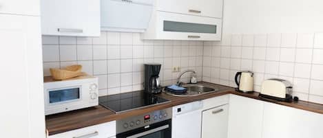 Een moderne keuken met witte kasten, een magnetron, een fornuis, een spoelbak en een broodrooster.