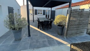 Un patio couvert avec une table et des chaises, entouré de plantes en pot et d’une clôture en bois.