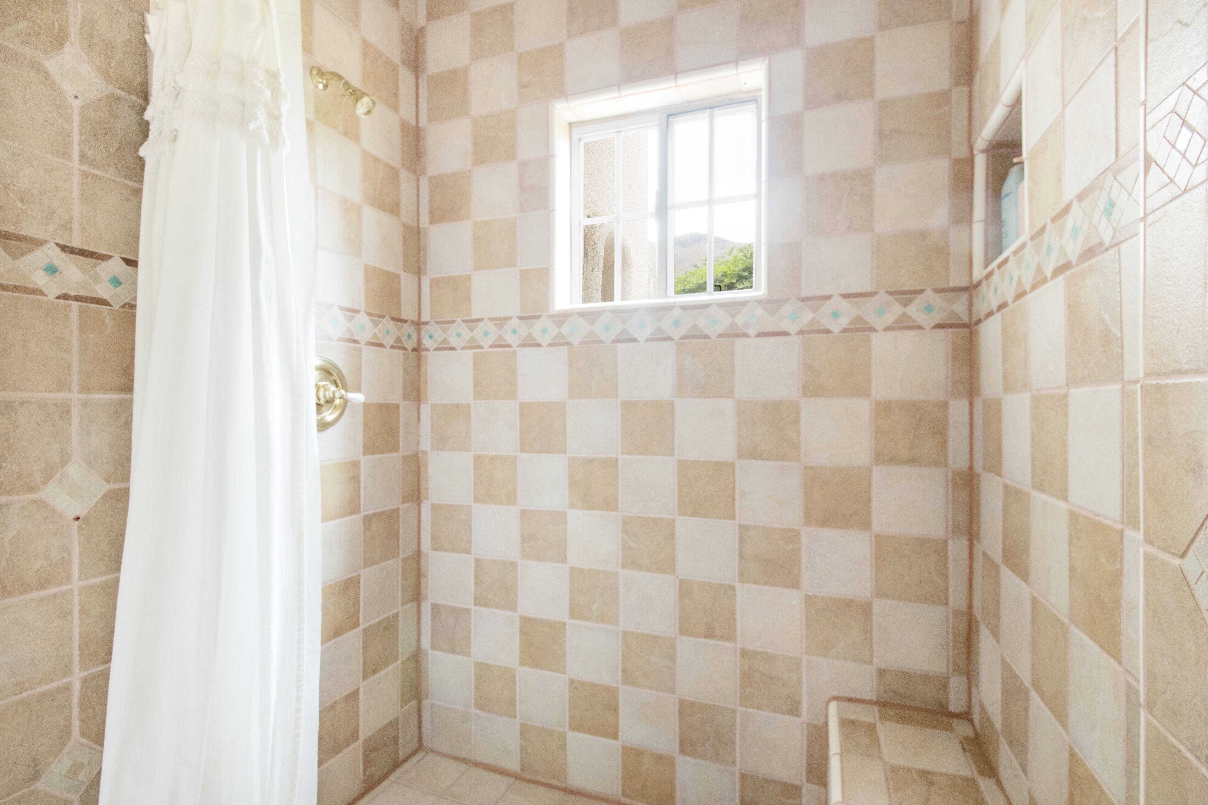 A bathroom with checkered tiles, a window, and a shower curtain.