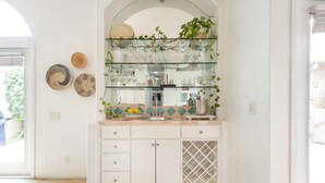 Uma cozinha com prateleira de vidro sobre a pia, armários brancos e painel de azulejos.
