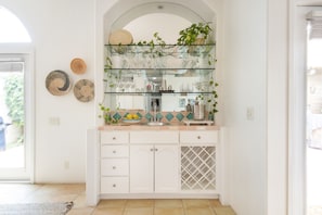 Una cocina con estante de vidrio sobre el fregadero, armarios blancos y salpicadero de azulejos.