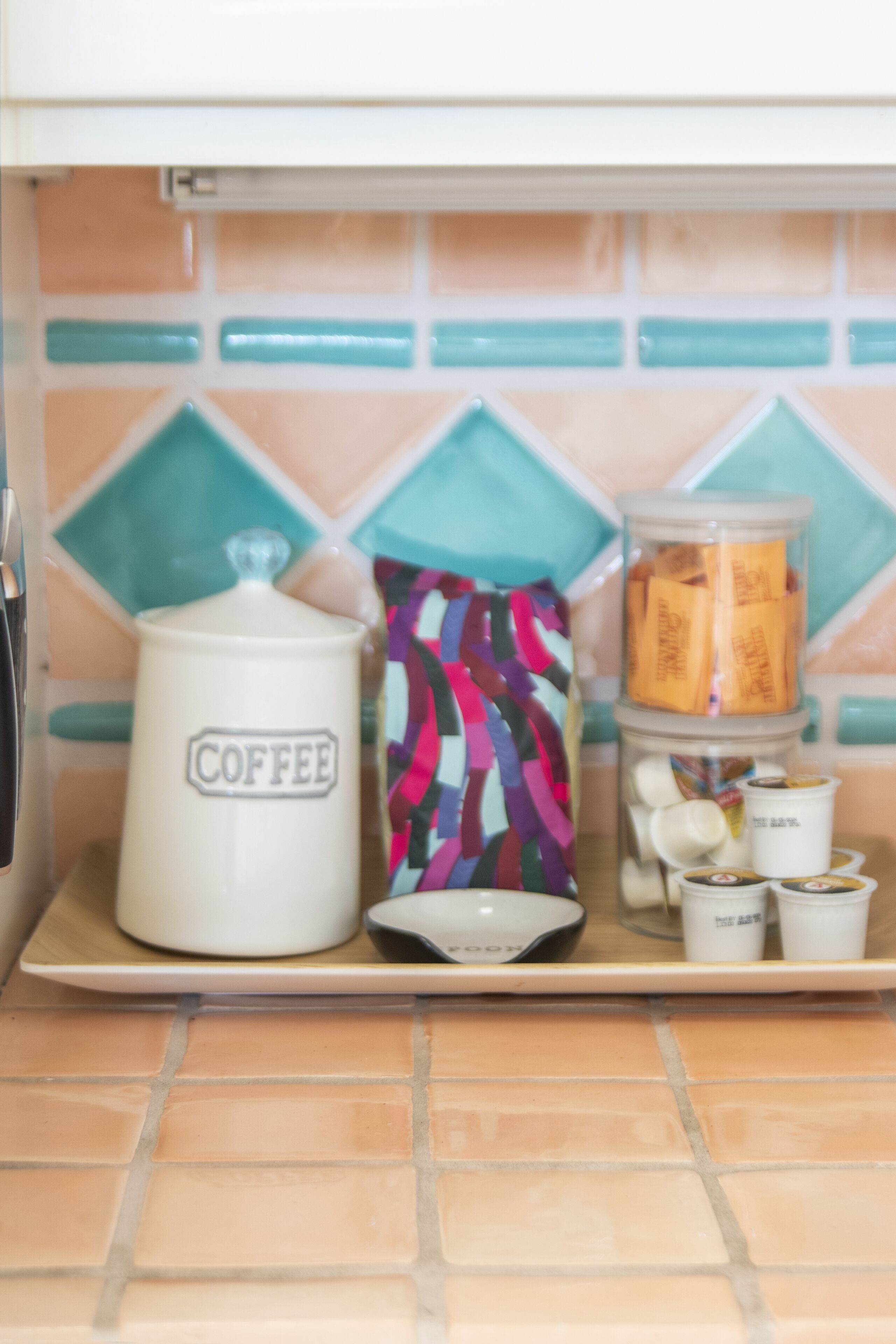 Un piano di lavoro in cucina con una macchina da caffè, una borsa colorata e un contenitore con del cibo.