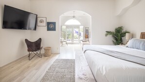 Quarto moderno com cama grande, televisão de tela plana na parede, uma poltrona confortável e vista para o exterior através de uma porta de vidro.