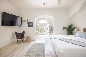 Un dormitorio moderno con una cama grande, un televisor de pantalla plana en la pared, un sillón cómodo y vistas al exterior a través de una puerta de vidrio.