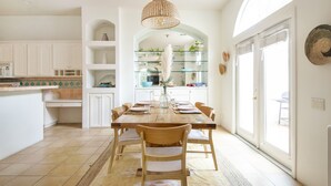 Uma cozinha espaçosa com armários brancos, uma mesa de jantar de madeira e uma grande janela que oferece luz natural.