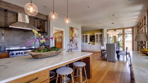 A modern kitchen with a large island, pendant lights, and a dining area with bar stools.