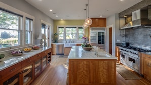 A modern kitchen with wooden cabinets, stainless steel appliances, and a large island with a bowl of fruit.