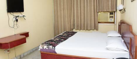 A hotel room with a bed, bedside table, TV, air conditioning unit, and curtains.
