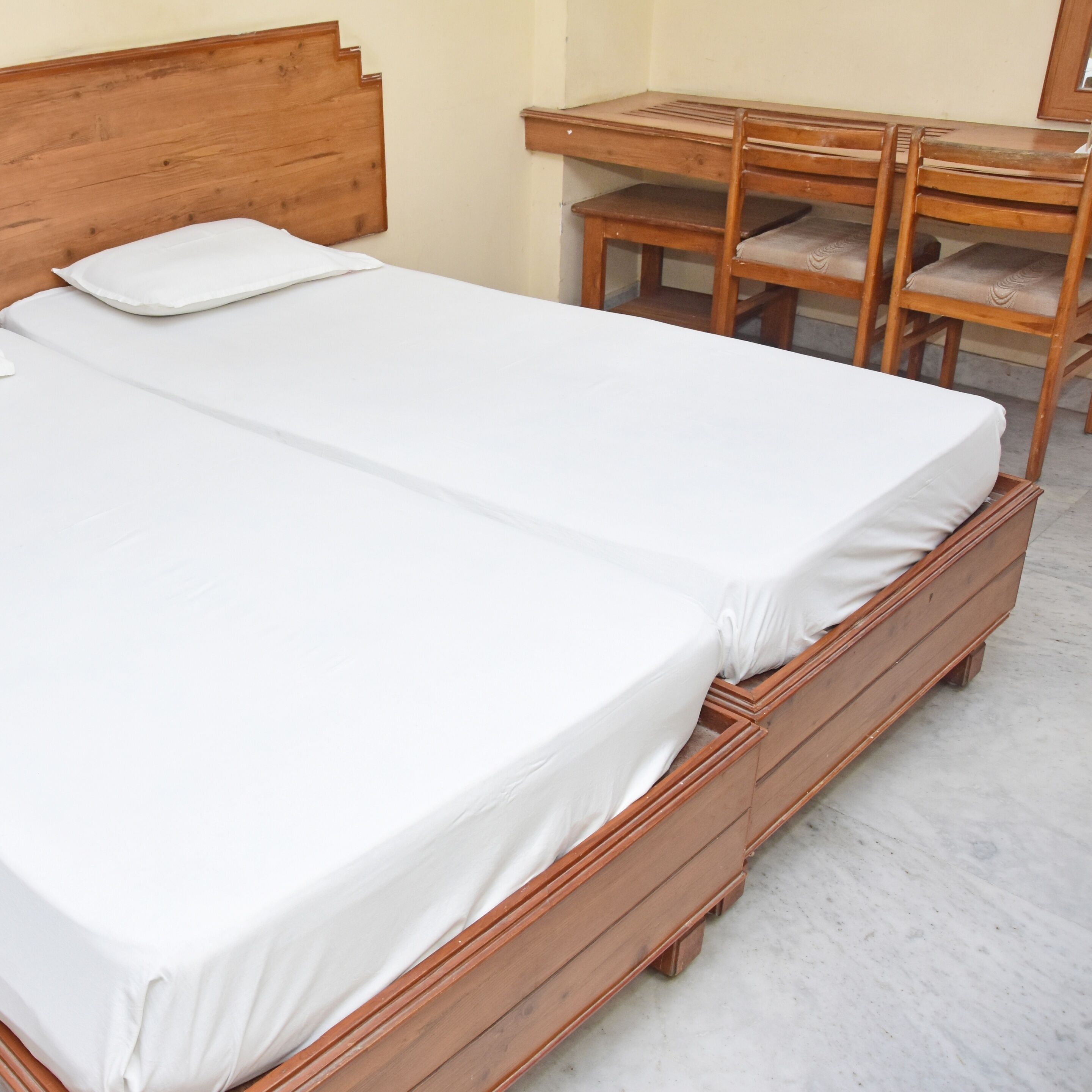 A double wooden bed with white bedding, a wooden nightstand, and a wooden chair with a cushioned seat.