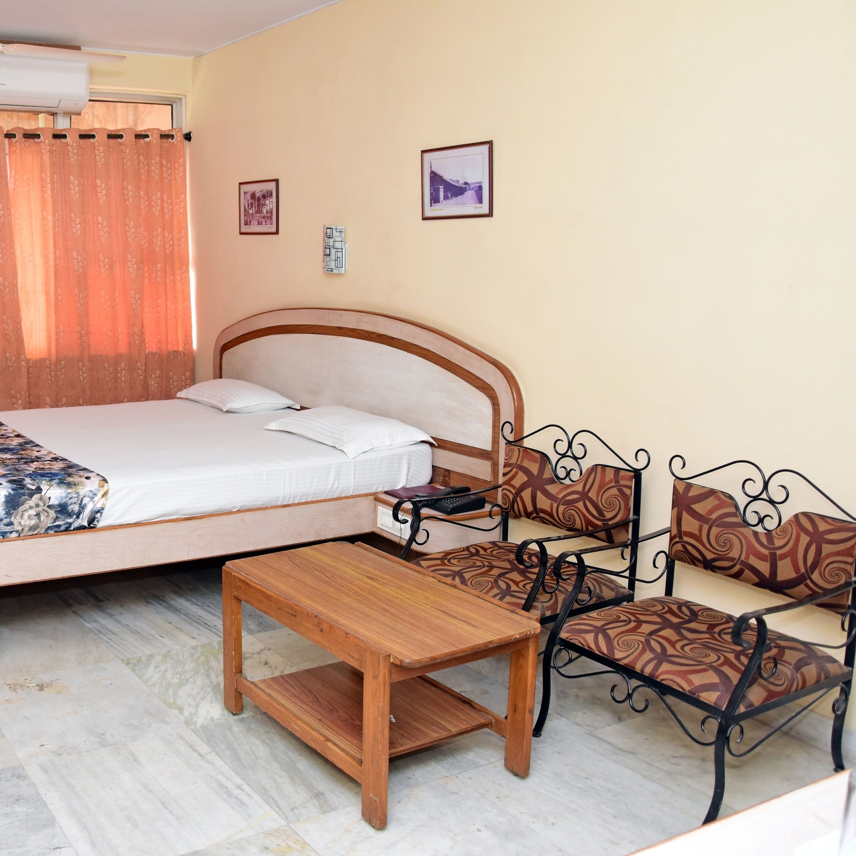 A bedroom with a bed, a wooden table, and a metal chair with a patterned cushion.