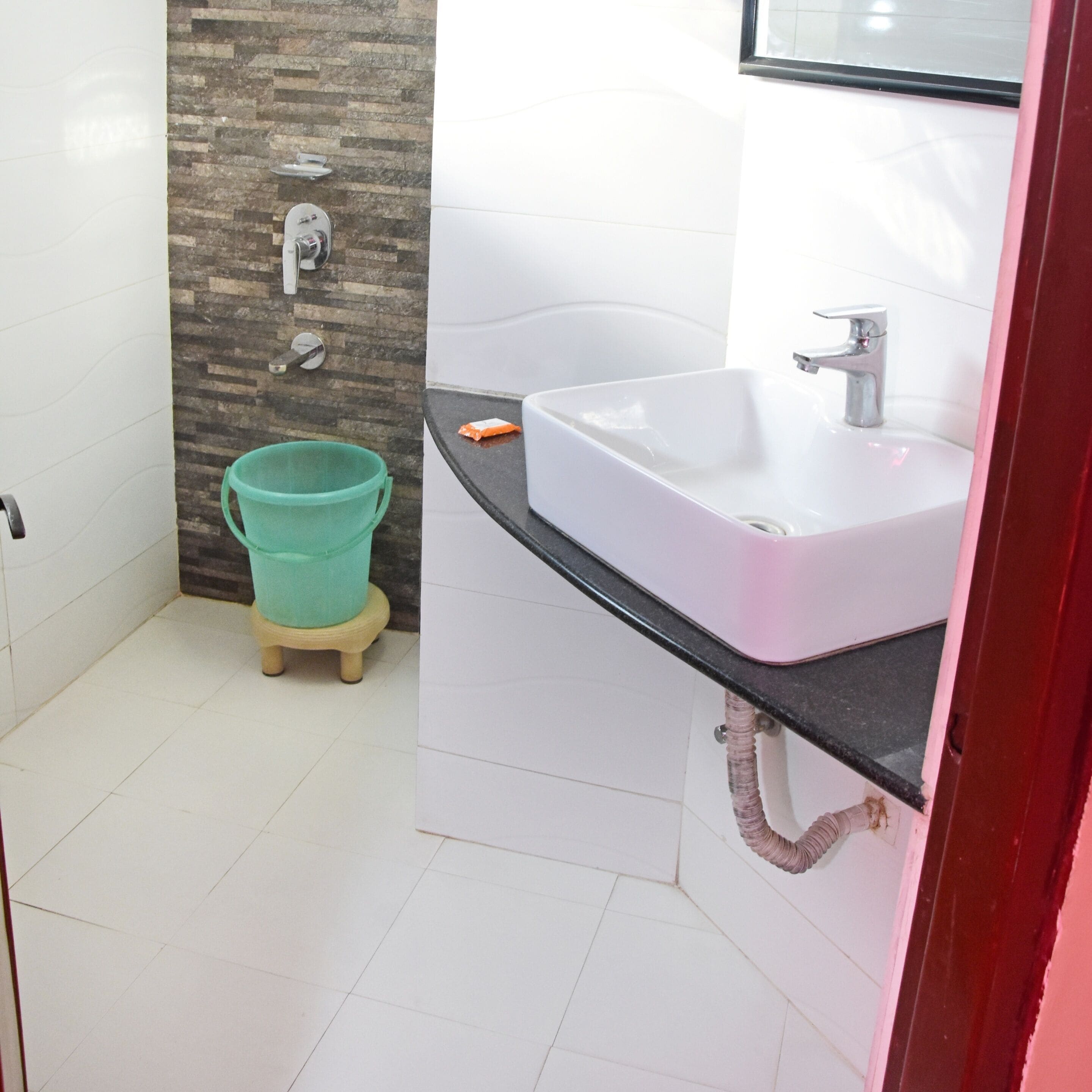 Un baño con un lavabo blanco, un cubo verde y piso de baldosas.