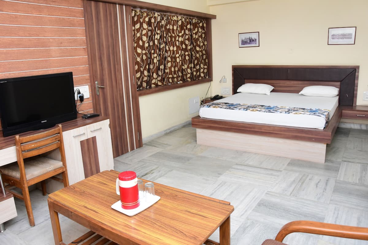 Una habitación de hotel con una cama, un televisor, un escritorio y una mesa con un vaso rojo.