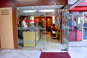 A reception area with a glass partition, a Coca-Cola refrigerator, and a seating area with tables and chairs. - Park Hotel (Bhopal)