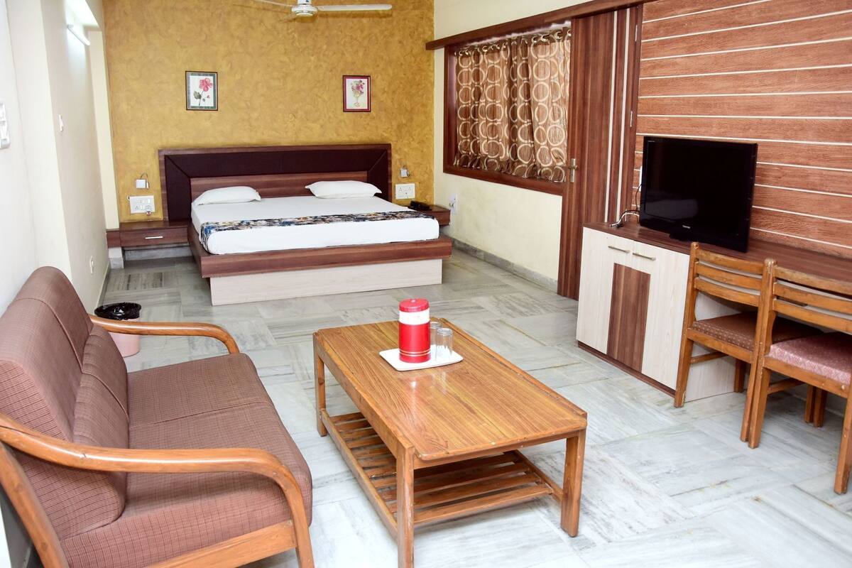 Habitación de hotel con cama, sofá, televisión y muebles de madera.