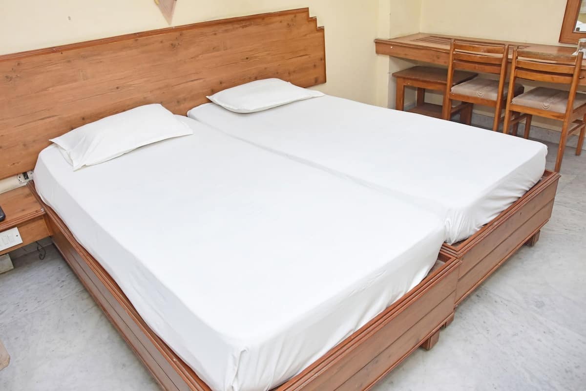 Una cama doble con sábanas blancas, un cabecero de madera y un escritorio de madera con sillas.