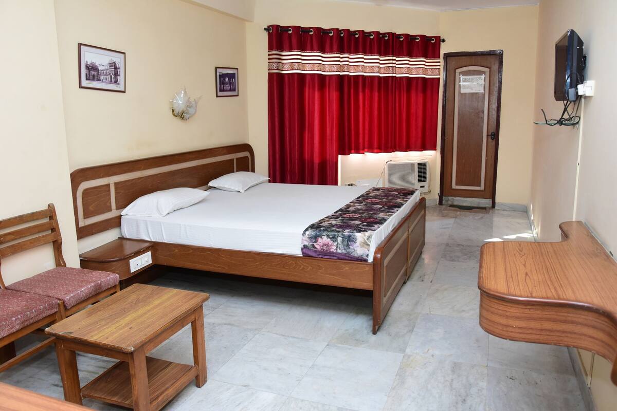 Habitación de hotel con cama de madera, un escritorio, una silla, un armario y un televisor montado en la pared.