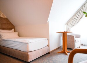 Une chambre d’hôtel moderne, équipée d’un lit, d’une petite table, d’une chaise et d’une fenêtre avec des rideaux.