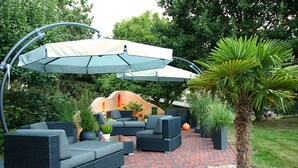 Eine Terrasse mit Gartenmöbeln, einer überdachten Sitzgelegenheit und einer Palme.