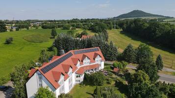 Een groot gebouw met een rood dak en zonnepanelen, omgeven door groene velden en bomen.