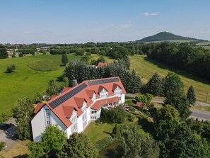 Un grand bâtiment doté d’un toit rouge et de panneaux solaires, entouré de champs verdoyants et d’arbres.